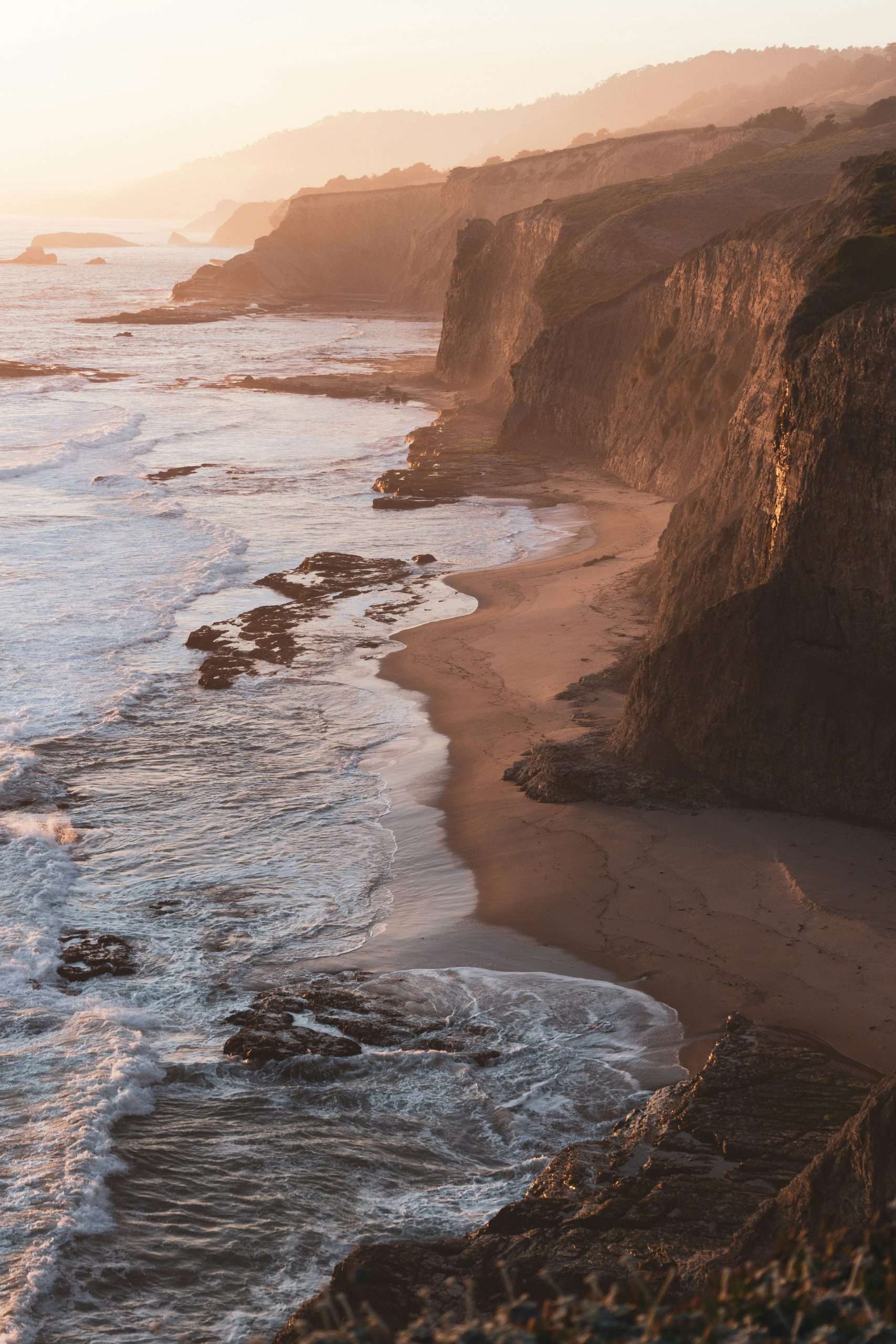 craig-melville-_JKymnZ1Uc4-unsplash Sunset over rugged coastal cliffs and ocean waves.