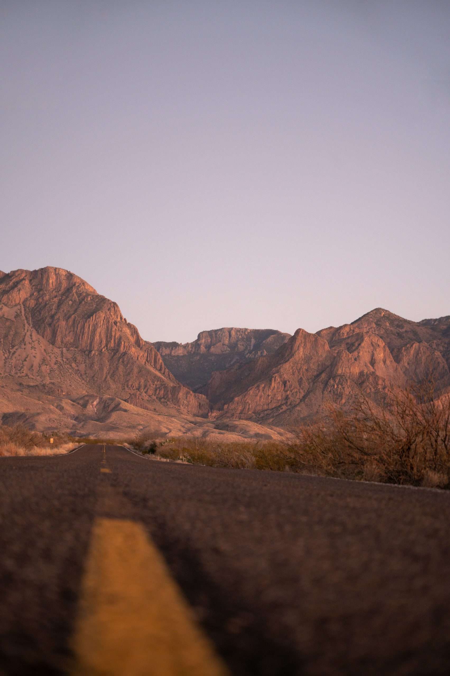 loik-marras-QPH1r-eIbto-unsplash Empty road leading to desert mountains at sunset.