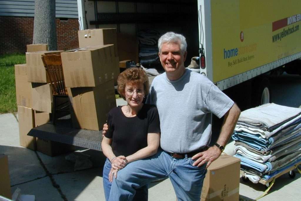 Couple smiling beside moving truck and boxes.